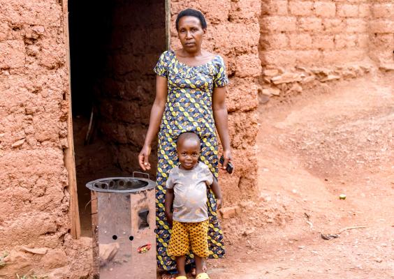 Valentine standing with her child beside the improved cooking stove she received through JP RWEE, which has reduced firewood use and eased daily cooking. Photo: FAO Rwanda/ Christian Ngabonziza