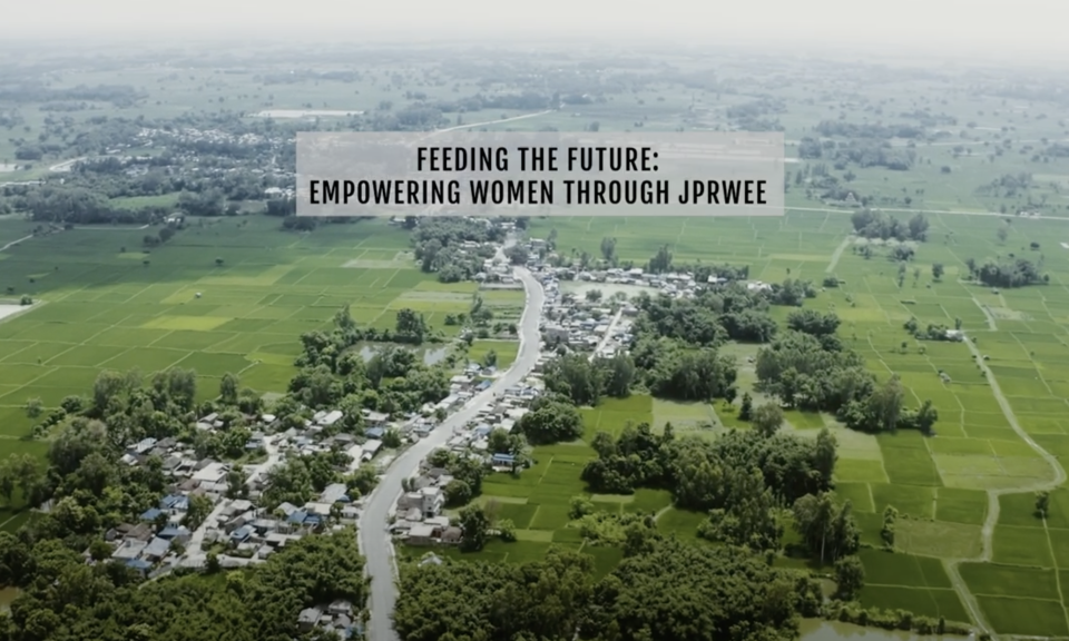 The image shows an aerial view of a rural landscape in Nepal, stretching far into the distance. There is an overlayed text that reads: "Feeding the Future: Empowering Women Through JPRWEE."